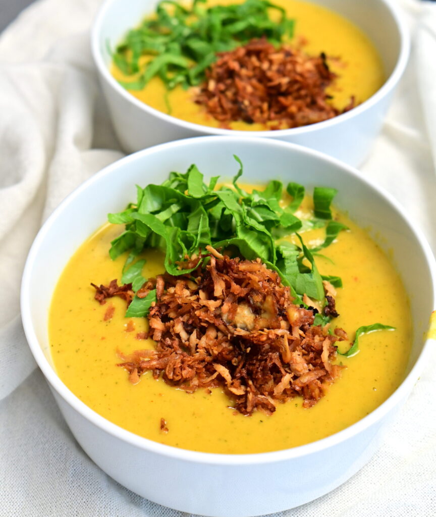 Two white bowls of creamy potato soup, topped with crispy tofu bacon and greens.