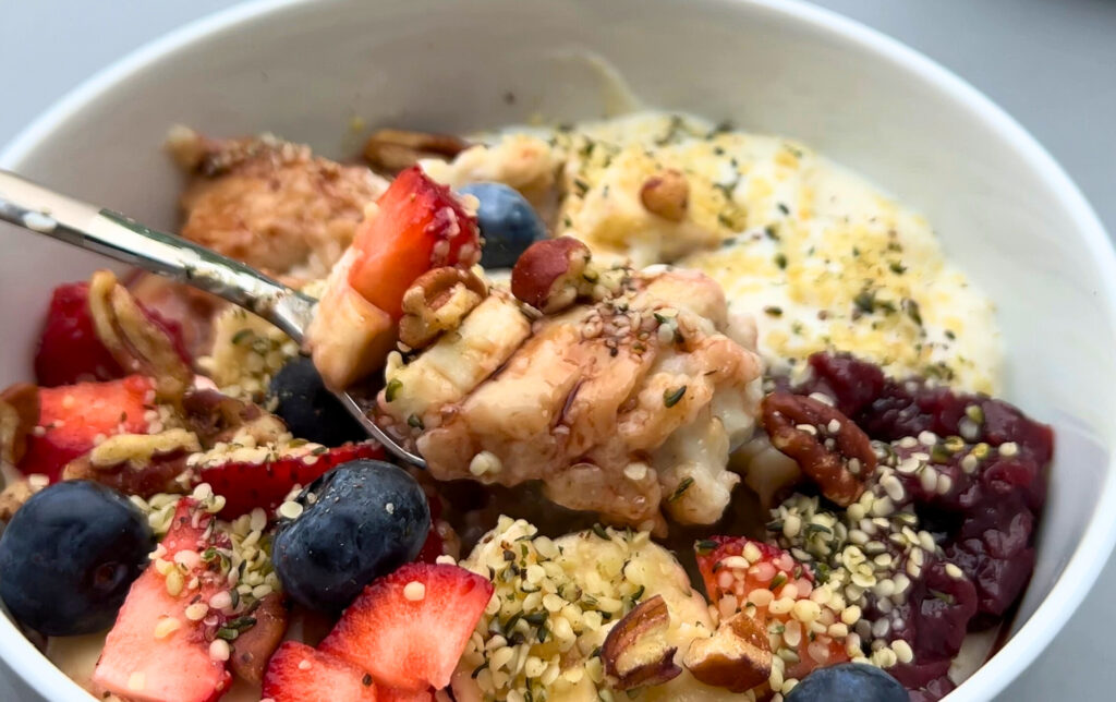 Cozy Morning Porridge Bowl with yoghurt, fruits, jam, hemp seeds, pecans, date syrup spoonful