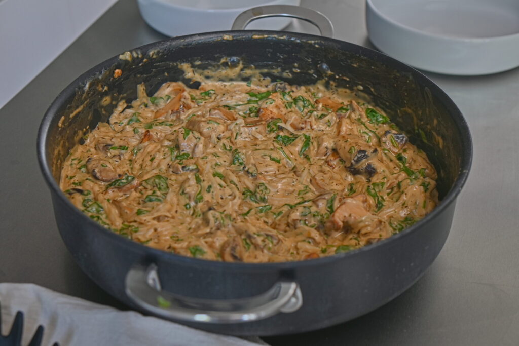 a wide pot on a metal surface and bowls, with gf rice noodles with mushroom sauce, herbs, creamy