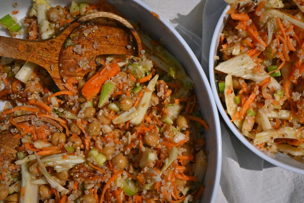 a serving bowl and small bowl with carrot and fennel salad and serving spoon on a table with white cloth