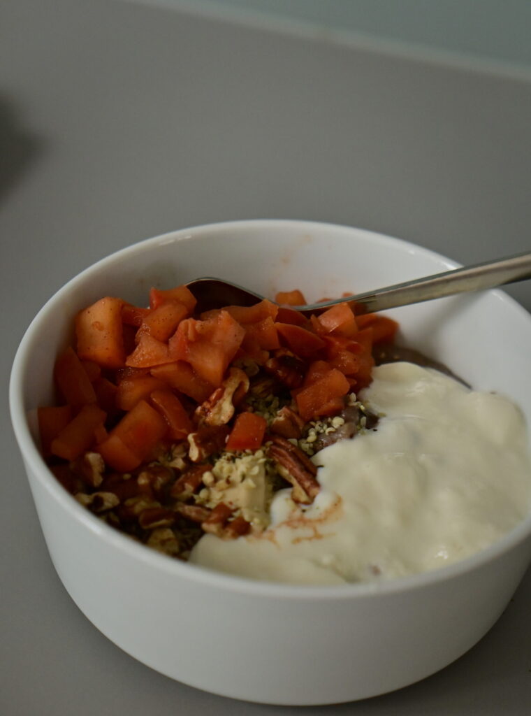 white bowl of oats with vegan soy yoghurt, pecans, caramelized cinnamon apples and fruits