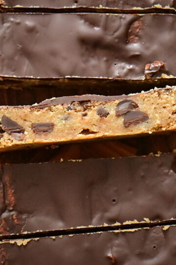chickpea Protein Cookie Dough bars covered with chocolate (one's side facing the camera) photographed from top and placed on a wooden cutting board