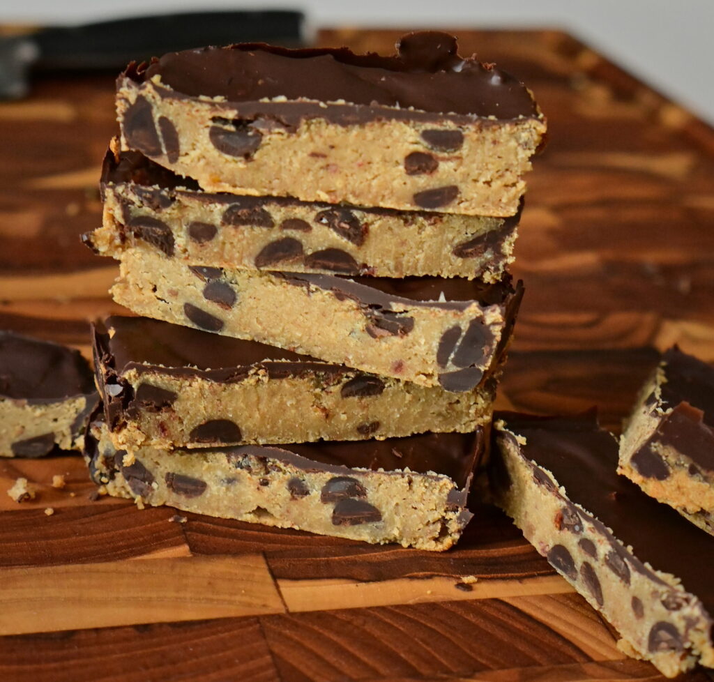 chickpea Protein Cookie Dough covered with chocolate, stacked on a wooden cutting board