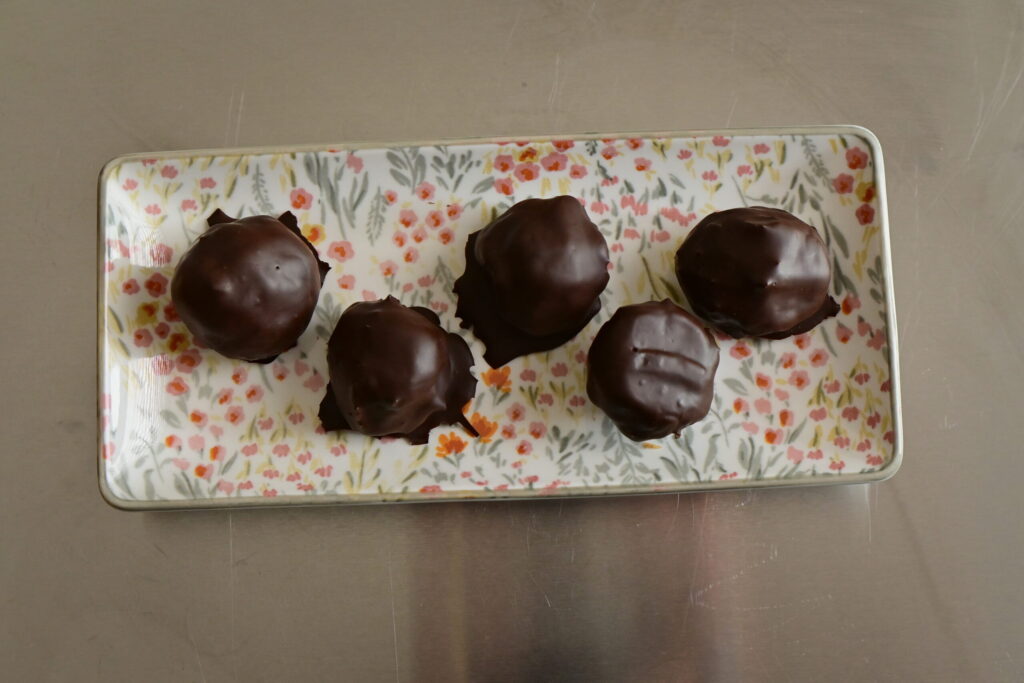 chickpea Protein Cookie Dough balls covered with chocolate on a flowered plate on a metal surface