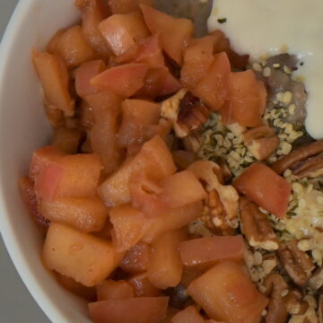 white bowl of oats with vegan soy yoghurt, pecans, caramelized cinnamon apples and fruits