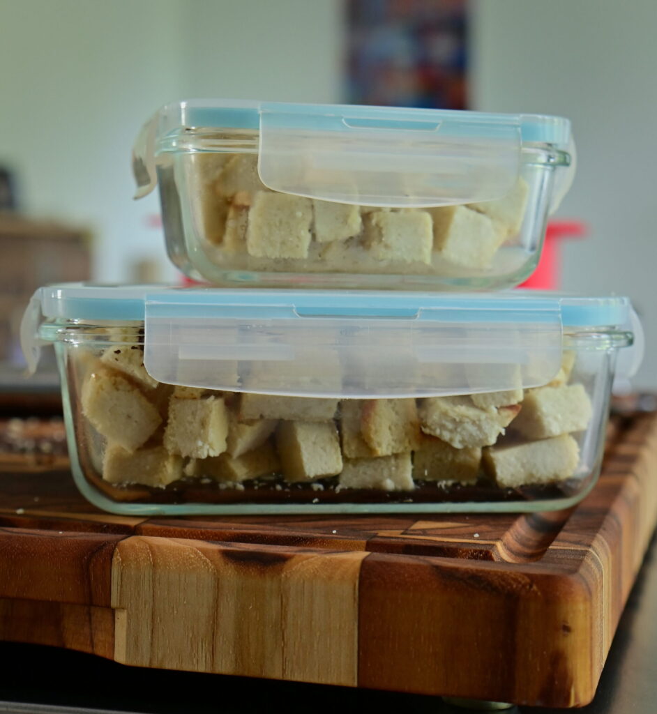 glass containers with almond feta cubes over a wooden board
