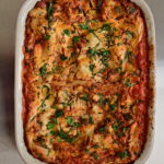 vegan lasagna with cashew bechamel and red zucchini + ground meat sauce in a red pan with basil leaves
