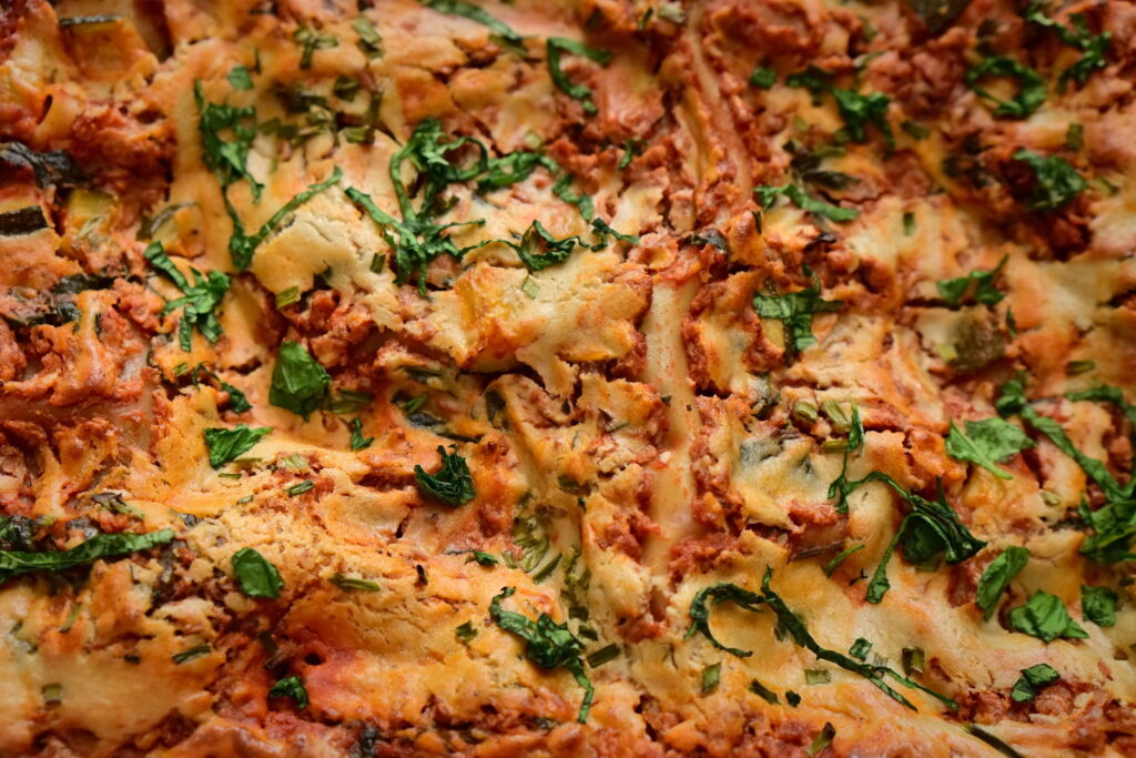 juicy vegan lasagna closeup with cashew bechamel and red zucchini + ground meat sauce with basil leaves