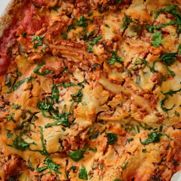vegan lasagna with cashew bechamel and red zucchini + ground meat sauce in a red pan with basil leaves