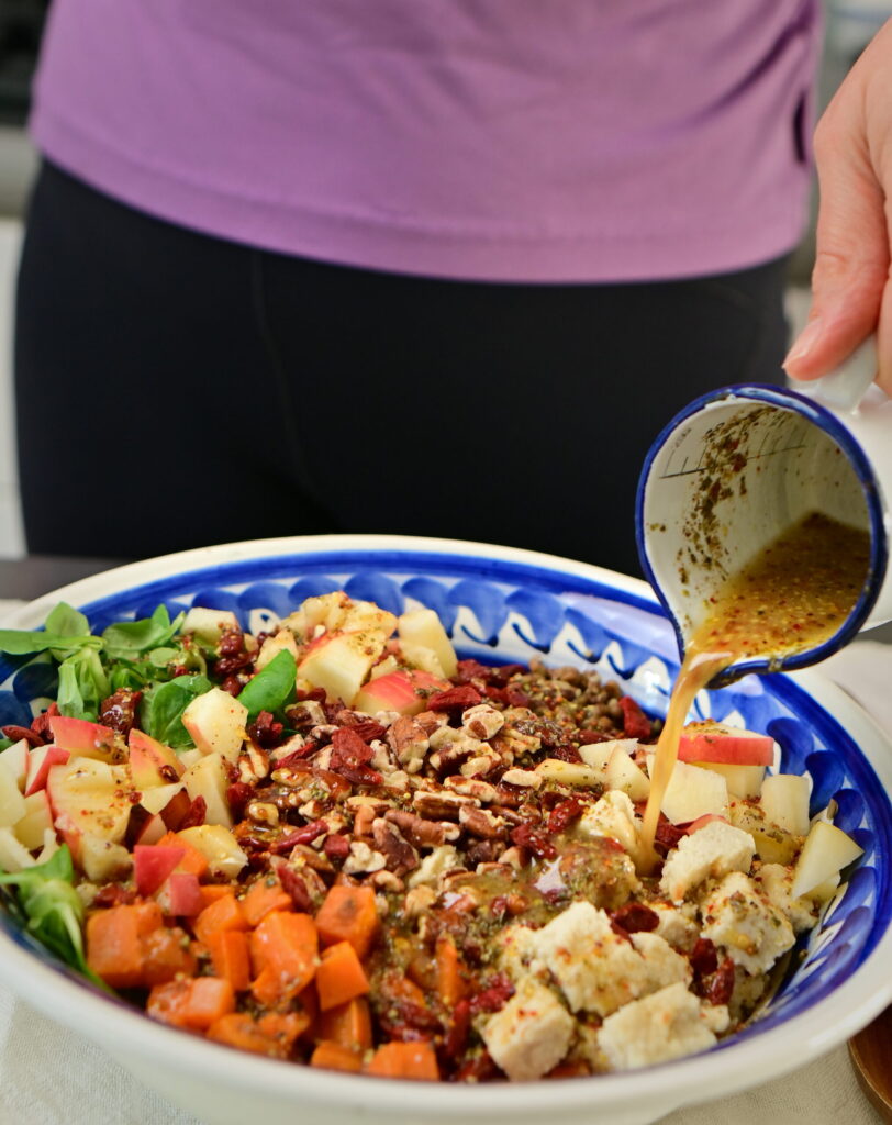 brown lentils and sweet potato salad with wooden spoons and blue bowl with sauce from a saucer dripping