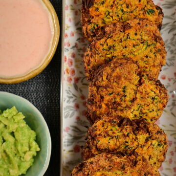 carrot and zucchini fritters in line on a flower pattern long plate, with 2 dips