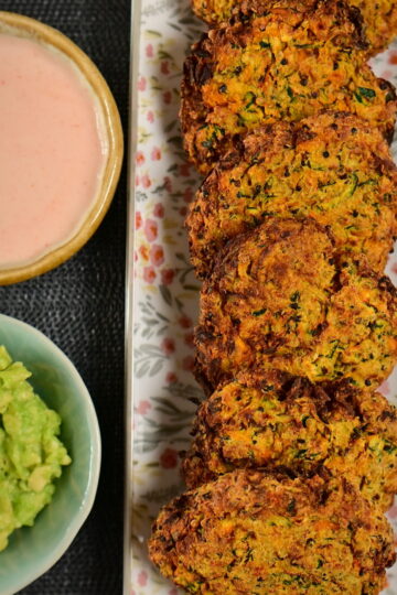 carrot and zucchini fritters in line on a flower pattern long plate, with 2 dips