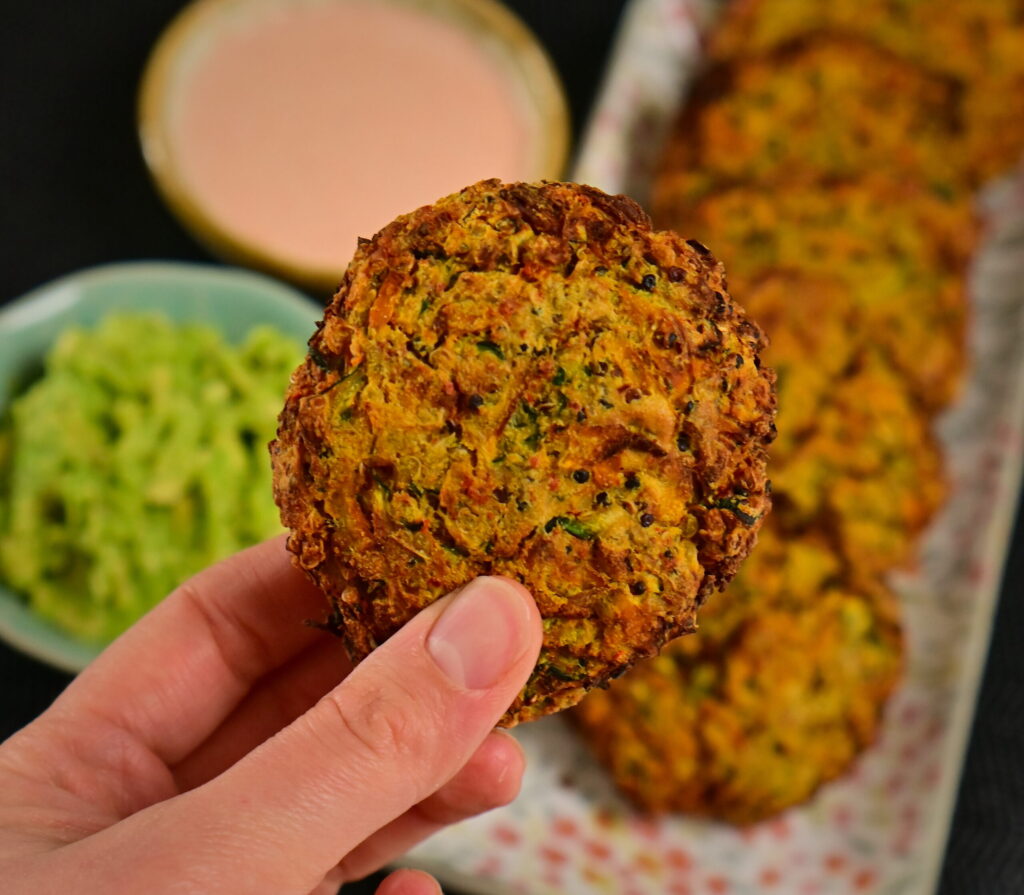 a fritter in front of - carrot and zucchini fritters in line on a flower pattern long plate, with 2 dips