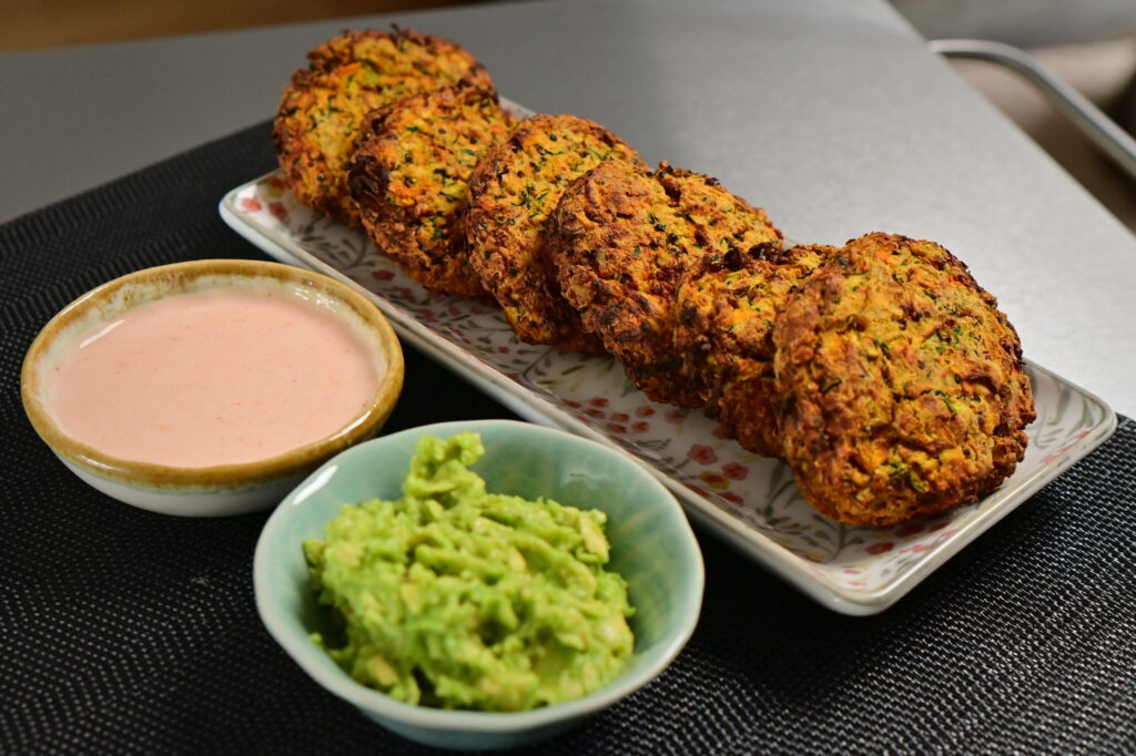 carrot and zucchini fritters in line on a flower pattern long plate, with 2 dips