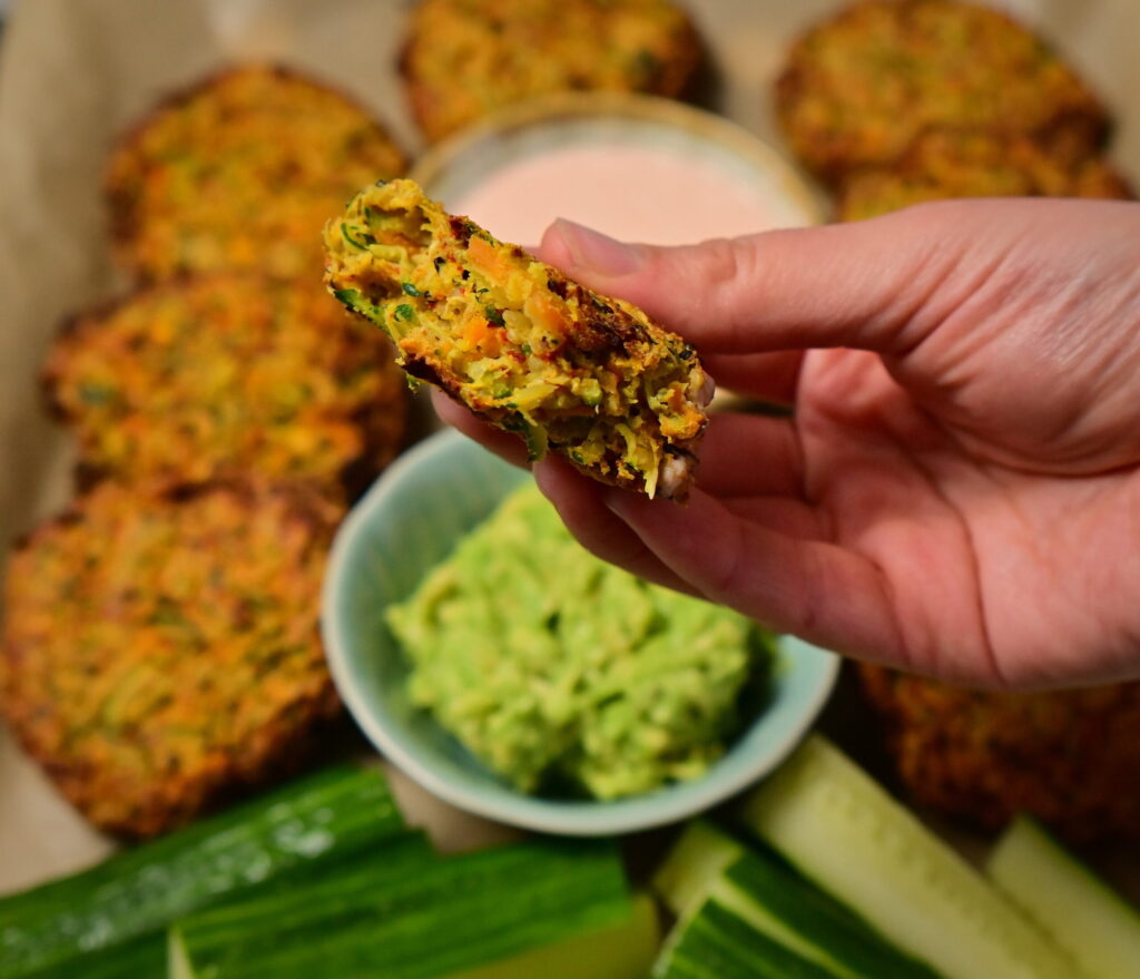 half a carrot and zucchini fritter in a orange deep next to guacamole, cucumbers and other fritters