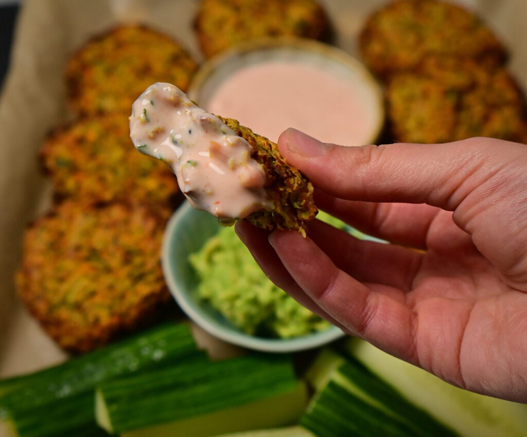 half a carrot and zucchini fritter in a orange deep next to guacamole, cucumbers and other fritters