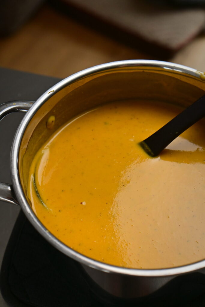 silky bright orange vegetables soup in a pot with a ladle