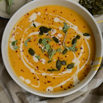 silky bright orange vegetables soup in a bowl, topped with pumpkin seeds, cream, sage and chilli.