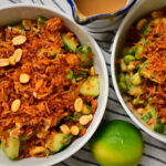 Two bowls of Thai-style crispy rice salad with lime and peanut sauce on a striped tablecloth