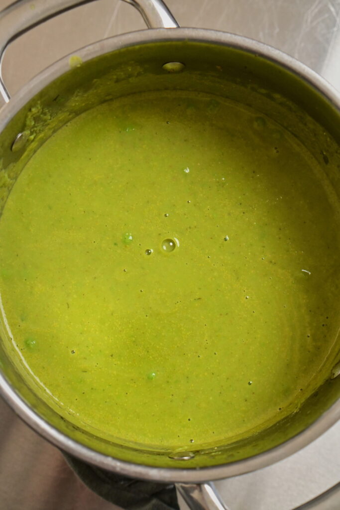 Stainless steel pot with thick green creamy pea soup.