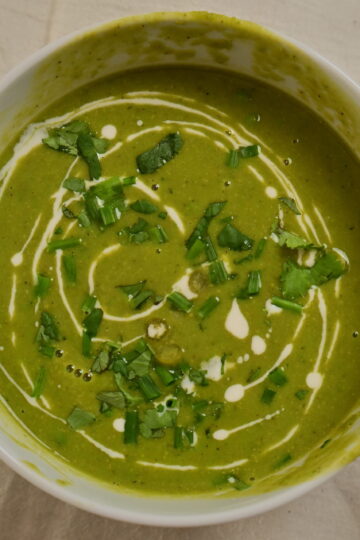 Bowl of creamy pea soup drizzled with cream and topped with herbs.