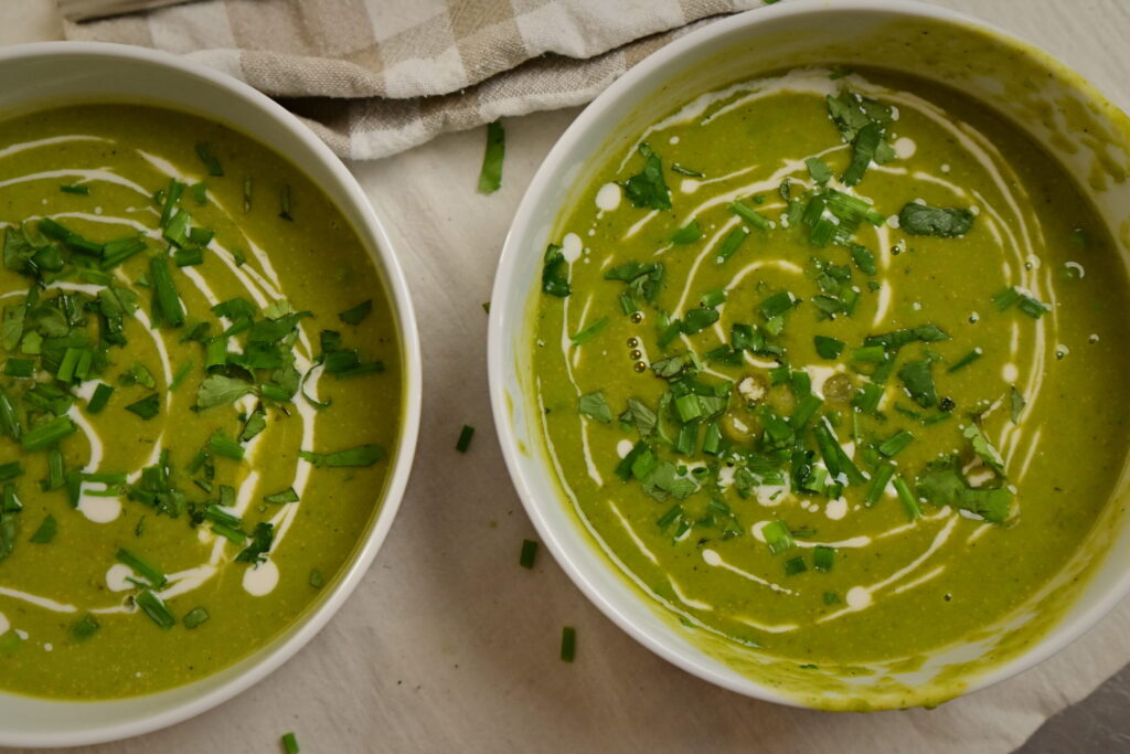 Two white bowls of creamy pea soup drizzled with cream and herbs