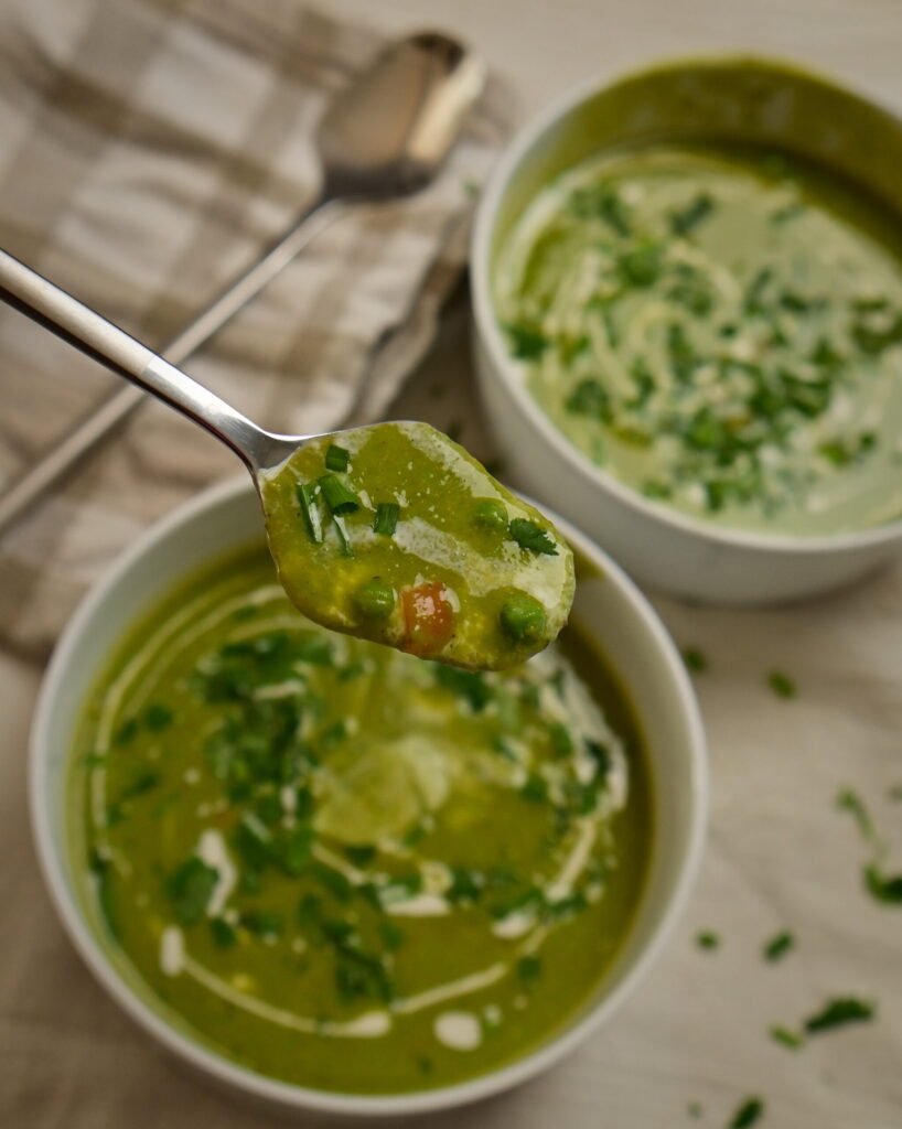 Two white bowls of creamy pea soup, with a spoon in front holding soup and carrot pieces.