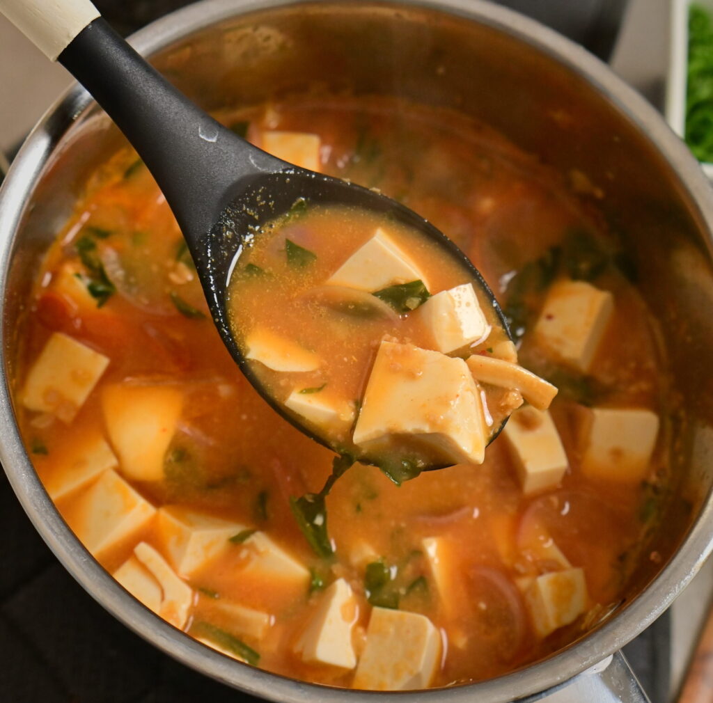 pot with vegan mapo tofu and steamed sushi rice in a side bowl, ladle with mapo tofu