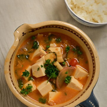 Clay bowl with vegan mapo tofu and steamed sushi rice in a side bowl, placed on a white cloth.
