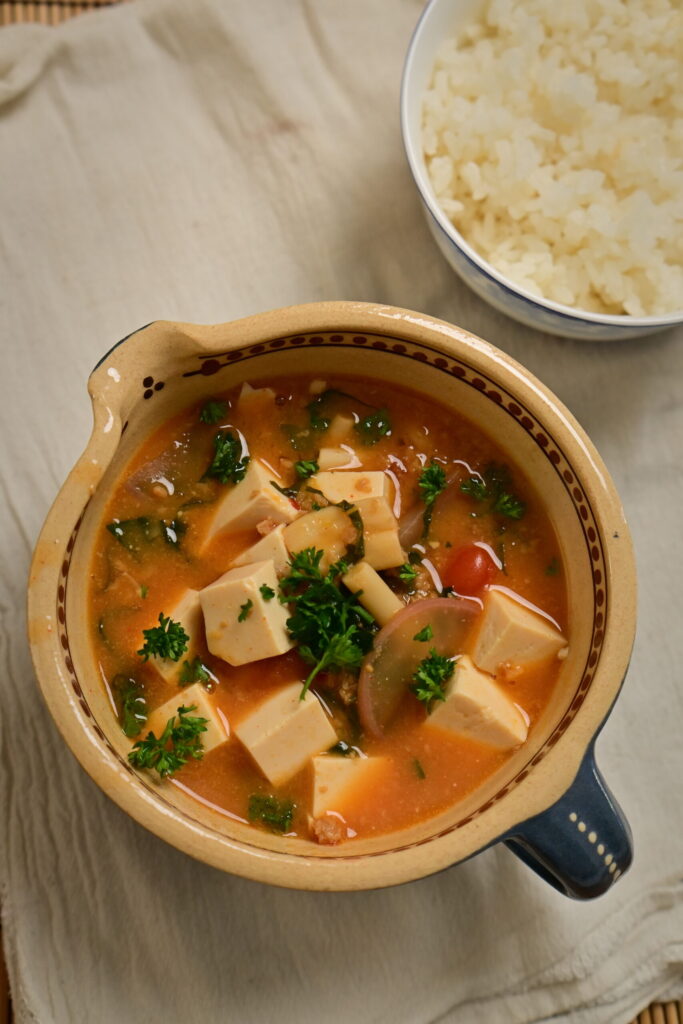 Clay bowl with vegan mapo tofu and steamed sushi rice in a side bowl, placed on a white cloth.