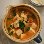 Clay bowl with vegan mapo tofu and steamed sushi rice in a side bowl, placed on a white cloth.