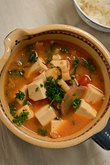 Clay bowl with vegan mapo tofu and steamed sushi rice in a side bowl, placed on a white cloth.