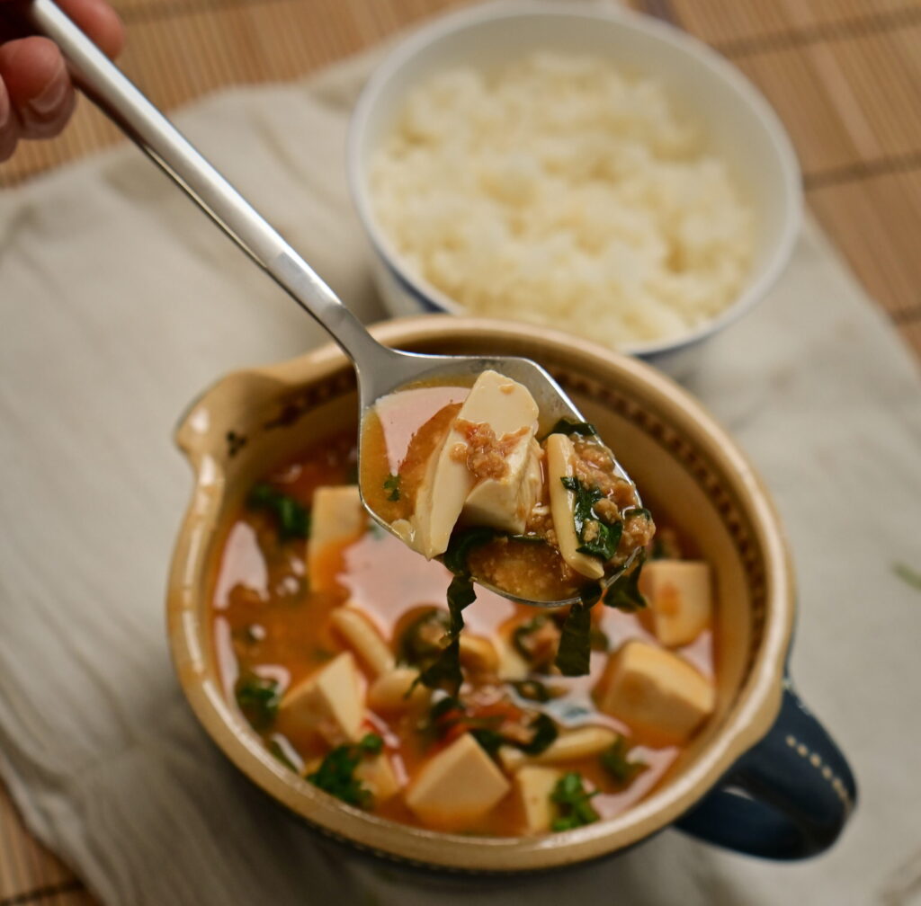 Clay bowl with vegan mapo tofu and steamed sushi rice in a side bowl, placed on a white cloth.