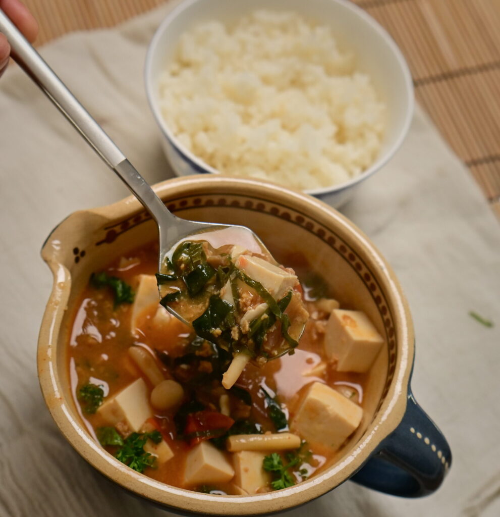 Clay bowl with vegan mapo tofu and steamed sushi rice in a side bowl, placed on a white cloth.