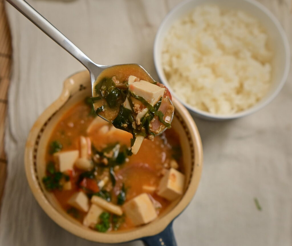 Clay bowl with vegan mapo tofu and steamed sushi rice in a side bowl, placed on a white cloth.