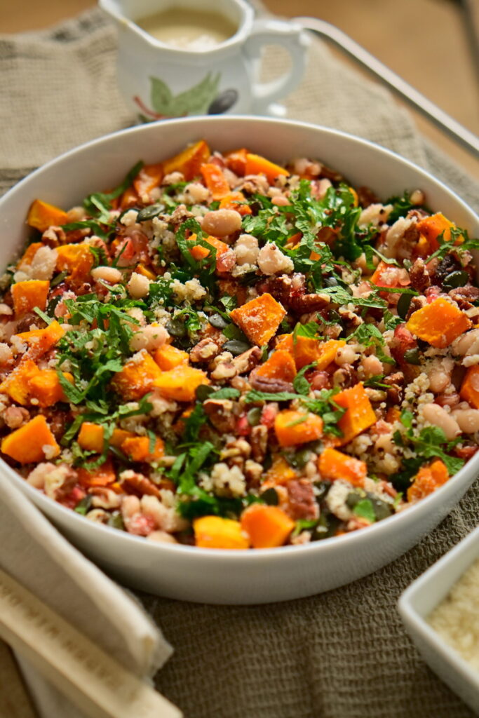 A serving bowl with kale salad, serving spoons, almond flour, on a brown tablecloth and a cream-colored cloth napkin