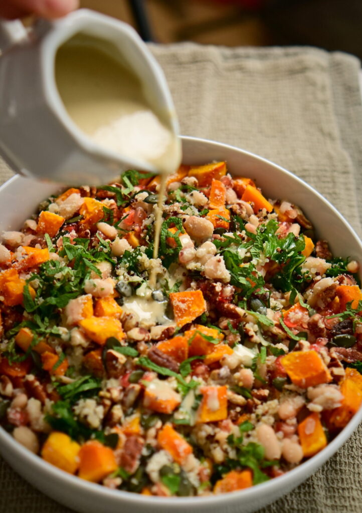 Pouring dressing over a kale and pumpkin salad from an elegant pitcher.