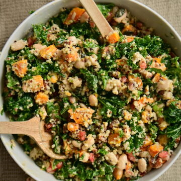 A serving bowl with kale and pumpkin salad, serving spoons, a pitcher, and almond flour on a brown tablecloth