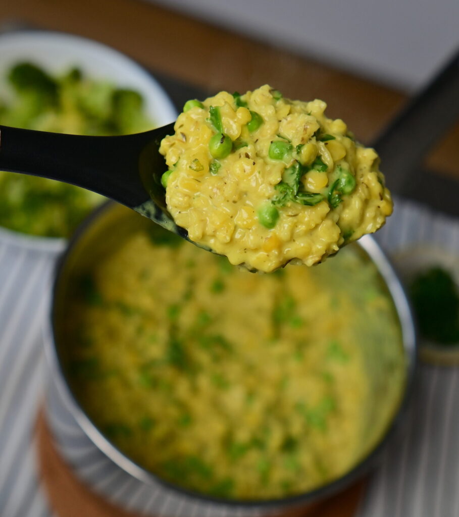 A ladle with Savory ״Cheesy" Oatmeal, with a pot and bowl in the background.