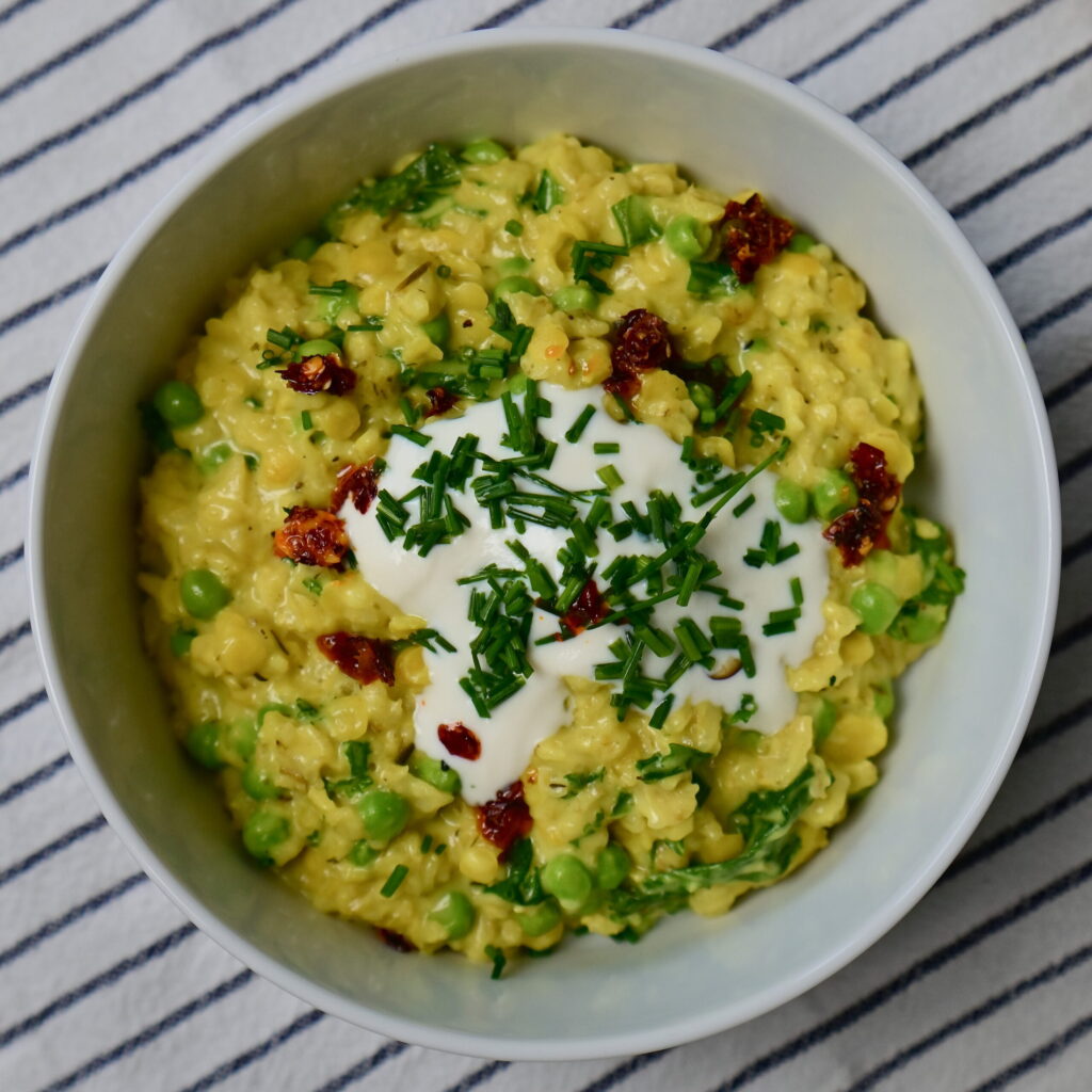A white bowl with Savory “Cheesy” Oatmeal, yogurt, chives, and chili oil, placed on a white cloth with blue stripes.
