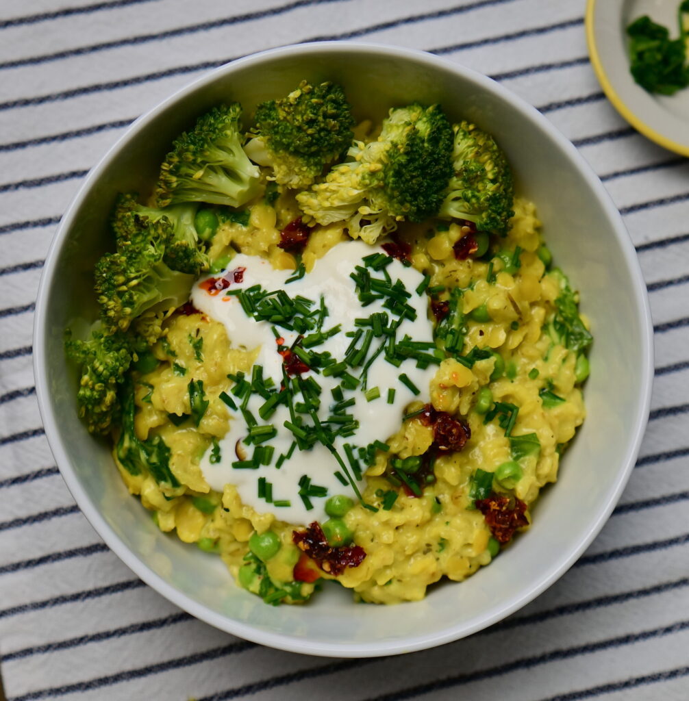A white bowl with Savory “Cheesy” Oatmeal, yogurt, chives, and chili oil, placed on a white cloth with blue stripes.