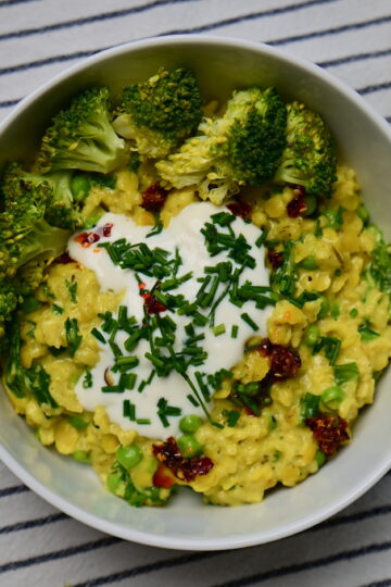 A white bowl with Savory “Cheesy” Oatmeal, yogurt, chives, and chili oil, placed on a white cloth with blue stripes.