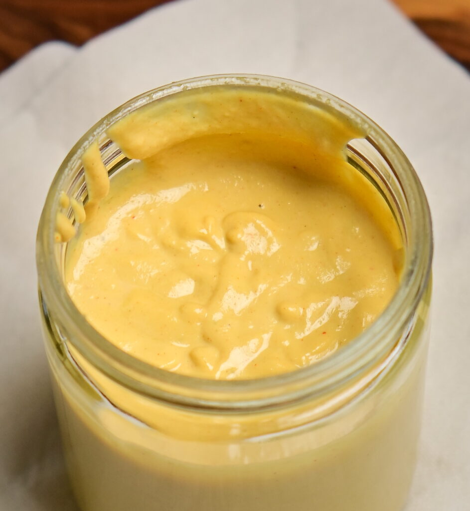 Yellow vegan cashew cheese sauce in a jar on a white cloth.