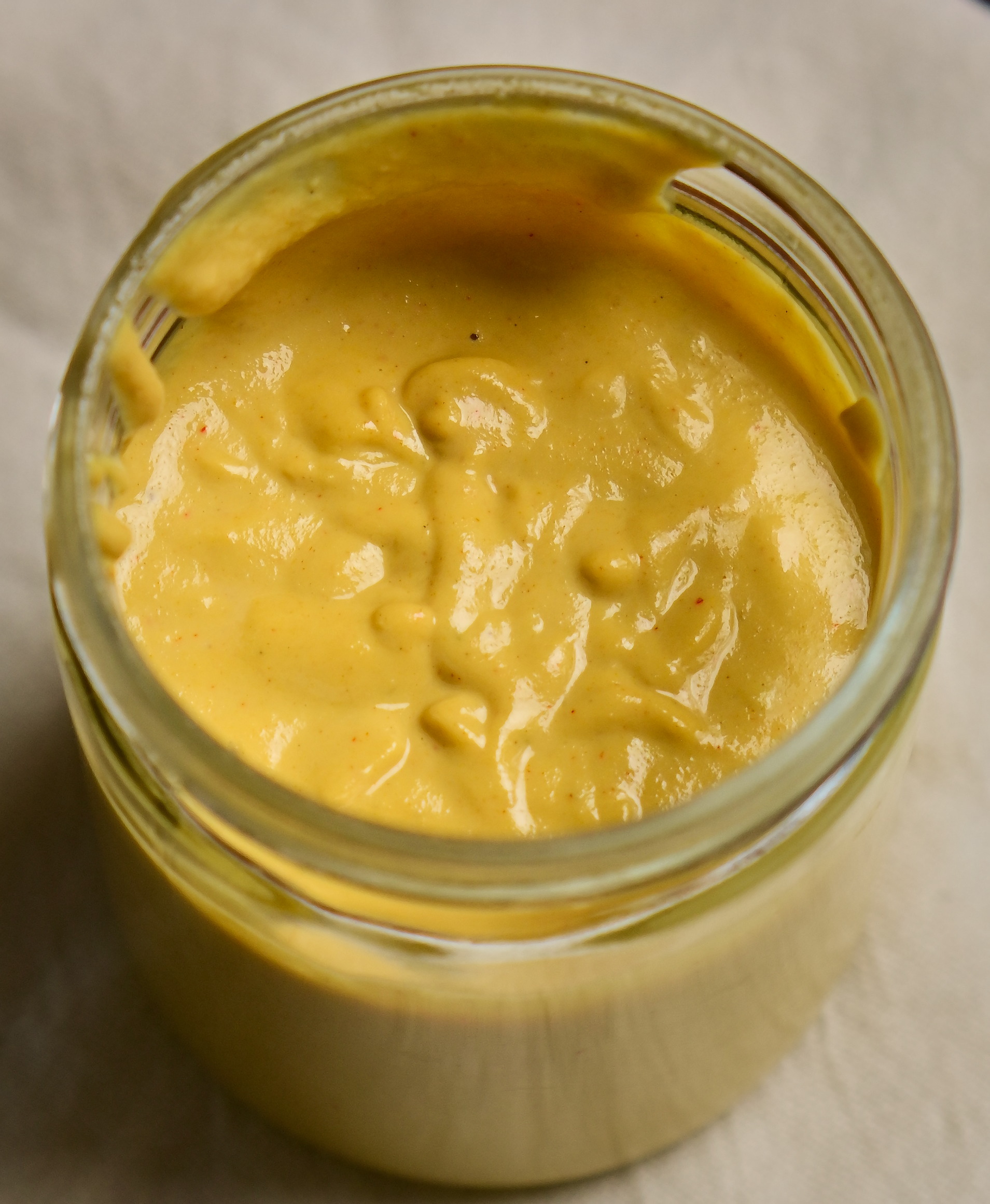 Yellow vegan cashew cheese sauce in a jar on a white cloth.