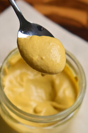 Yellowish vegan cashew cheese sauce on a spoon, with a jar underneath.
