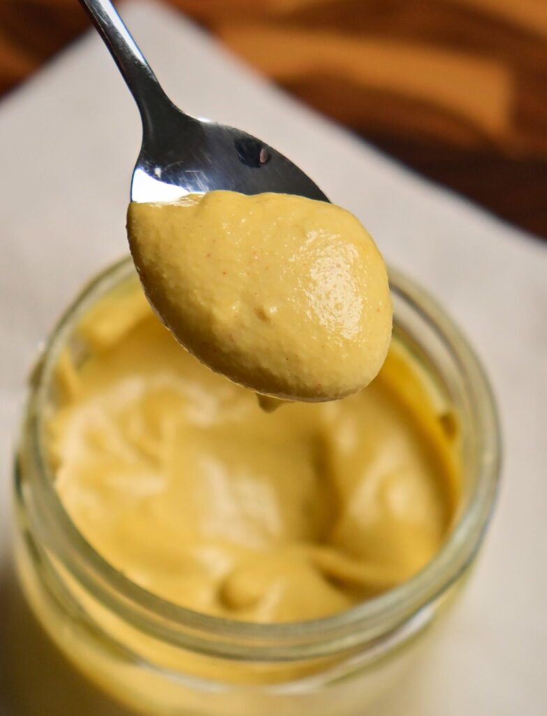 Yellowish vegan cashew cheese sauce on a spoon, with a jar underneath.
