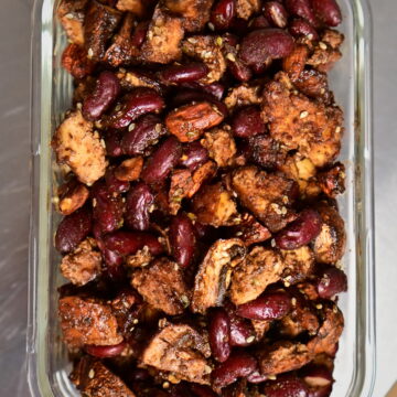 Protein mix of tofu, mushrooms, red beans, and seasoned baked almonds in a glass container on a metal surface.