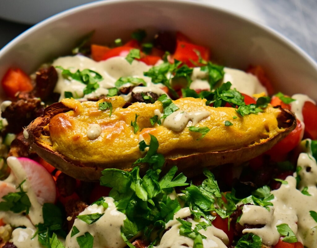 Vegan cashew cheese sauce drizzled over roasted sweet potato and salad, topped with tahini and chopped parsley.