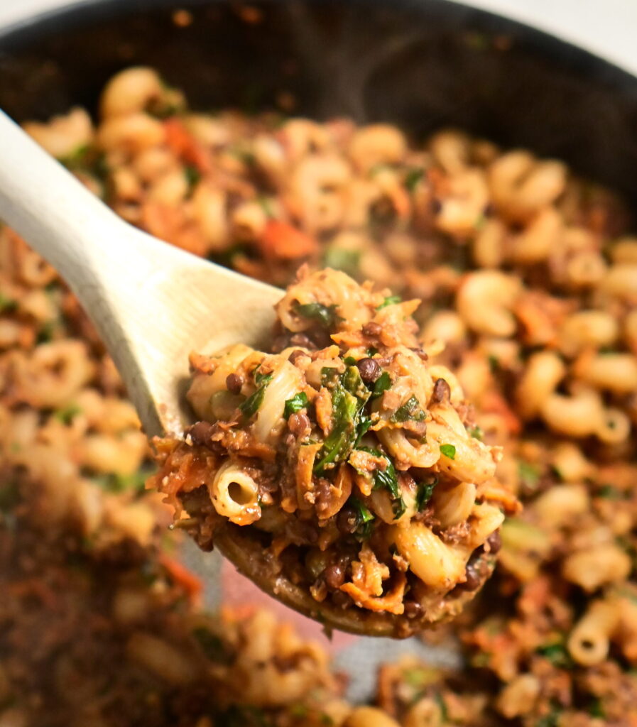 spoon with lentil and mushroom ragù with curly pasta, over a pot