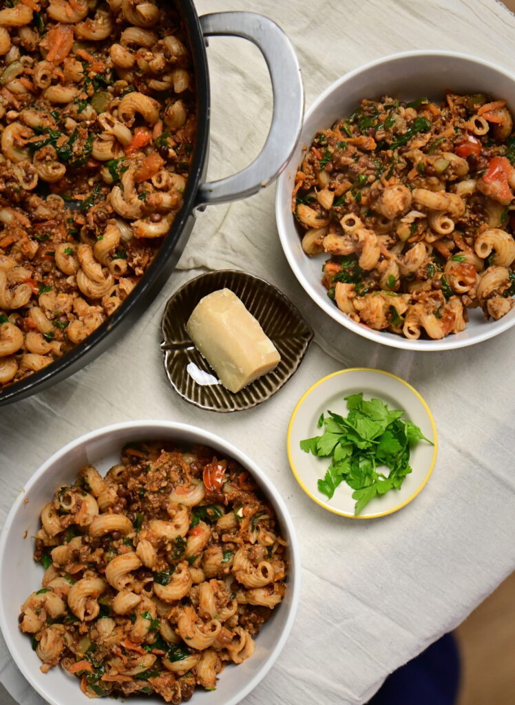 Two bowls and a pot of lentil and mushroom ragù with curly pasta.